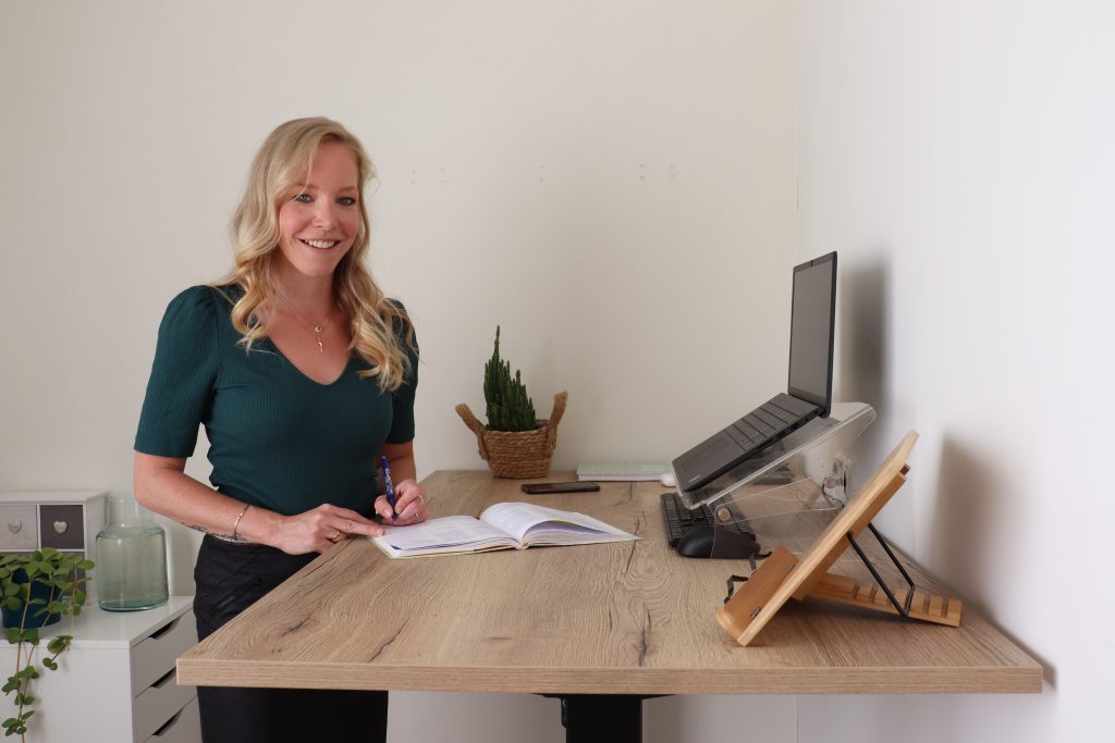 Gerrianne staat aan haar bureau en kijkt je glimlachend aan.